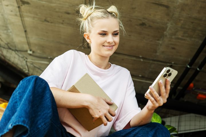 Mladé dievča pozerá na mobilný telefón a drží balík