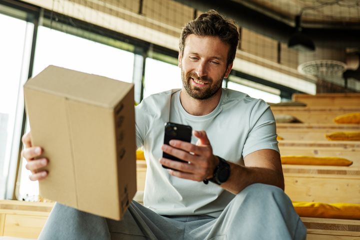 Muž pozerá na mobilný telefón a drží balík