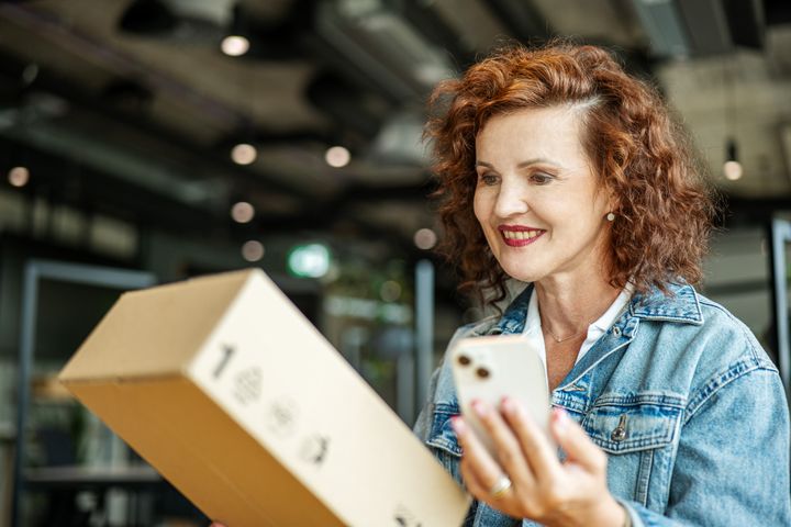 Staršia žena pozerá na balík a drží mobilný telefón