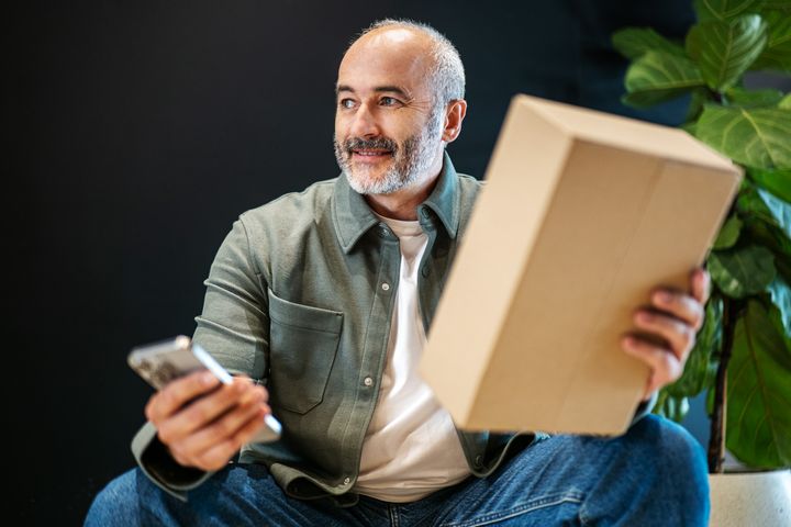 Starší muž drží mobilný telefón a balík