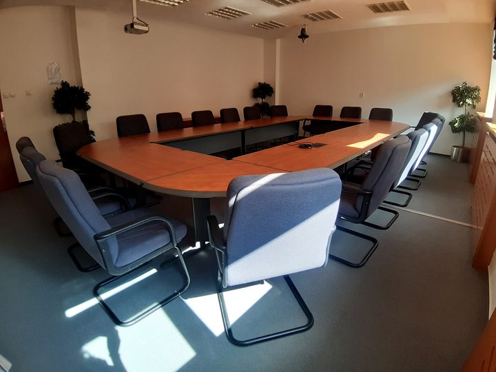 Konferenčná miestnosť s projektorom, stolom do tvaru O a stoličkami